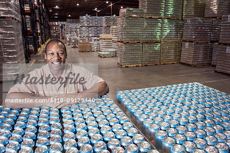 Portrait of an African American male warehouse foreman in a warehouse full of cans of flavoured water stored on pallets in the warehouse of a bottling plant.