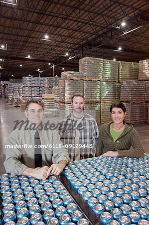 Portrait of two male and female Caucasian warehouse workers and a Caucasian male management person in a warehouse full of cans of flavoured water stored on pallets in the warehouse of a bottling plant.