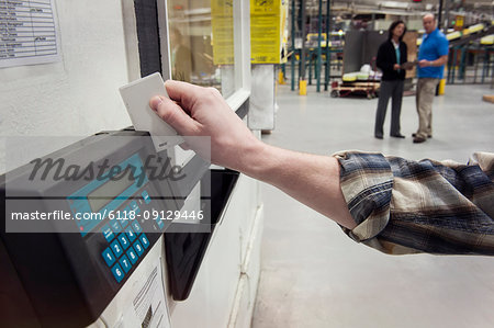 Close up of a hand checking in for work in a warehouse using a card key and a time clock to check in.