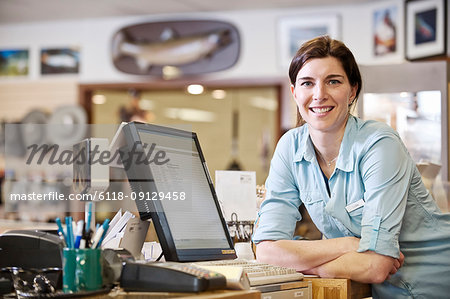 Portrait of a female Caucasian owner next to the computer at the front desk of a fly-fishing shop.
