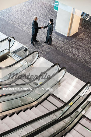 Mixed race pair of business people on the way to a meeting near a set of escalators.