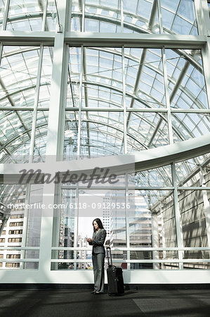 View of a Caucasian business woman in a suit coat standing in a covered glass walkway.