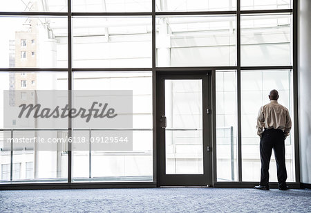 Businessman standing looking through a window in a large lobby area