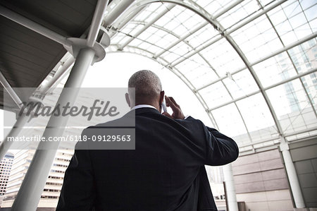 Black businessman on the phone while walking through a large glass covered walkway.