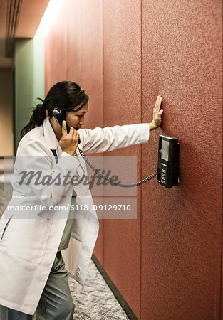 Asians woman doctor on a phone in a hospital lobby.