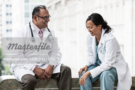 Hispanic man and Asian woman doctors conferring over a case in a hospital.
