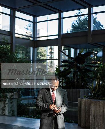 Black business man texting in a large lobby waiting area.