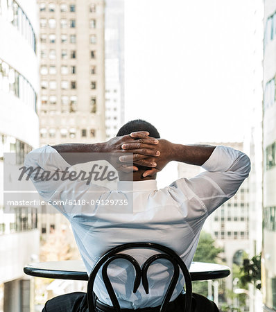 Black business man sitting at a lobby table looking at the cityscape through a large window.