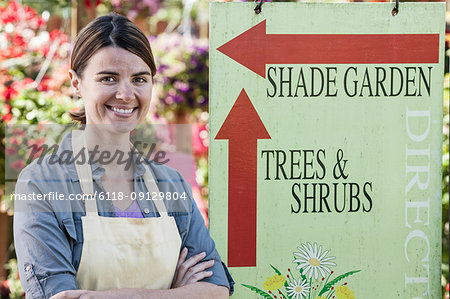 Young Caucasian woman employee of a garden centre nursery standing by an information sign.
