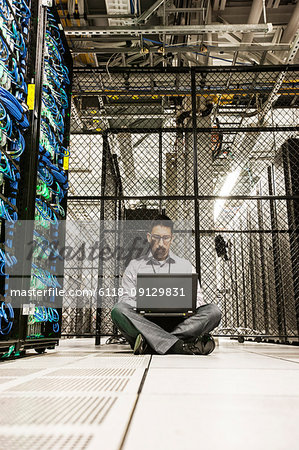 Hispanic man technician doing diagnostic tests on computer servers in a large server farm.