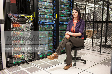 Caucasian woman technician sitting in an aisle of a large computer server farm.