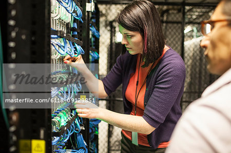 Caucasian woman and man technicians working on CAT 5 cables in a large computer server farm.