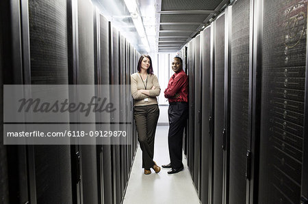 Caucasian woman and black man technician team in an aisle of a computer server farm.