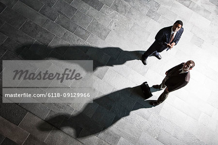 View from above of two businessmen and shadows on the floor of a business lobby.