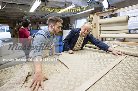 Young Caucasian man learning the art of upholstery from a senior male upholsterer.