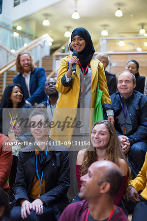 Smiling woman in hijab talking with microphone in conference audience
