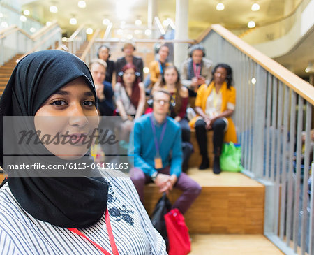 Portrait confident female speaker in hijab with audience in background