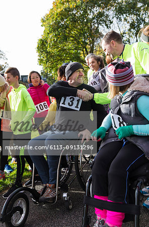 Man in wheelchair shaking hands with runner in crowd at charity race