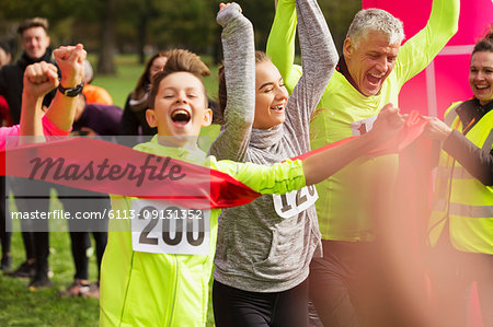 Enthusiastic boy runner crossing charity run finish line with family