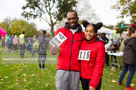 Portrait smiling, confident father and daughter runners with marathon bibs at charity run in park