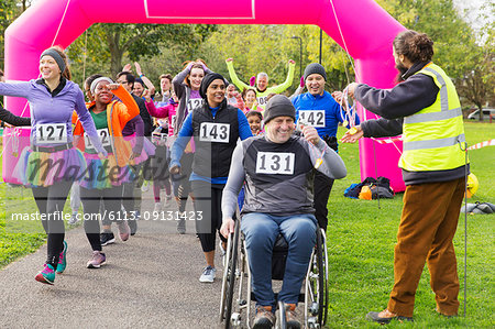 Man in wheelchair and runners receiving medals, crossing charity race finish line