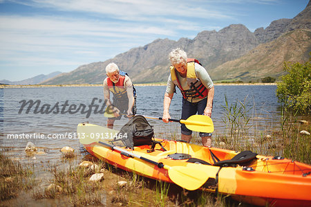 Active senior couple preparing kayak at sunny, summer lake