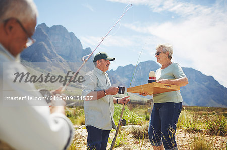 Active senior woman serving coffee to husband fishing