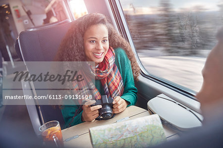 Smiling young woman with camera and map riding passenger train