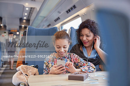 Mother and daughter sharing headphones, listening to music with smart phone on passenger train