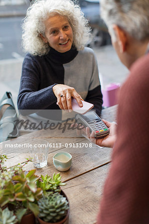Woman using smart phone contactless payment at cafe