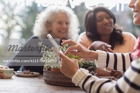 Smiling women friends with smart phone in cafe