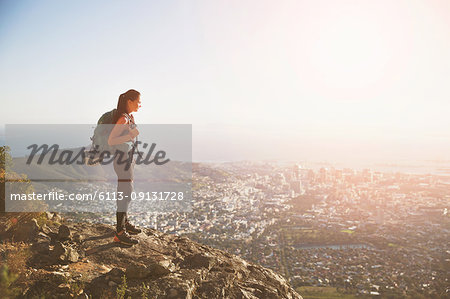 Female rock climber on top of hill overlooking sunny city
