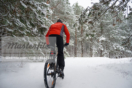 Cyclist in Red Riding the Mountain Bike in the Beautiful Winter Forest. Extreme Sport and Enduro Biking Concept.