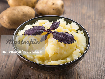 Mashed potatoes with fresh red basil in dark bowl on wooden background. Copy space.