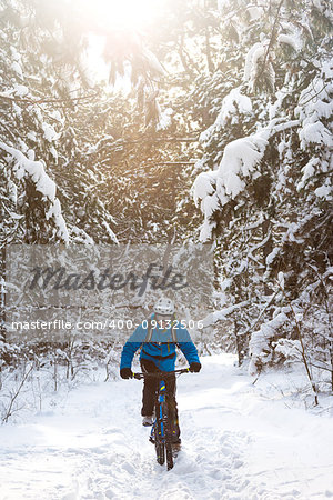 Cyclist in Blue Riding the Mountain Bike in the Beautiful Winter Forest Lit by the Sun and Covered with Snow. Extreme Sport and Enduro Biking Concept.