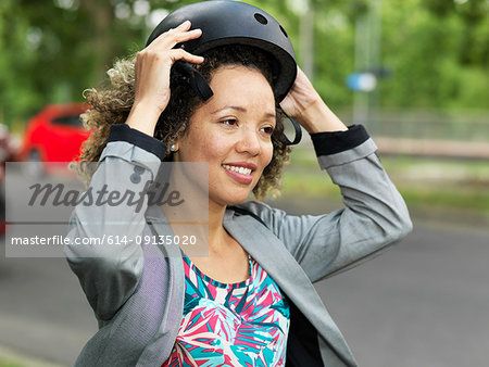 Mid adult woman putting on bicycle safety helmet
