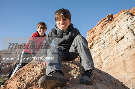 Portrait of boys sitting on rock looking at camera, sticking out tongue, Lone Pine, California, USA