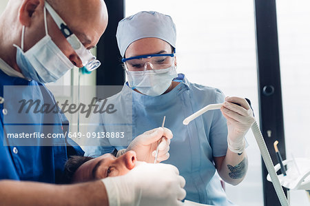 Dentist and dental nurse carrying out dental procedure on male patient, close-up