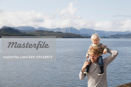 Man giving son shoulder ride by fjord, Aure, More og Romsdal, Norway
