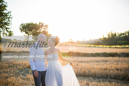 Heterosexual couple standing in field, face to face, smiling