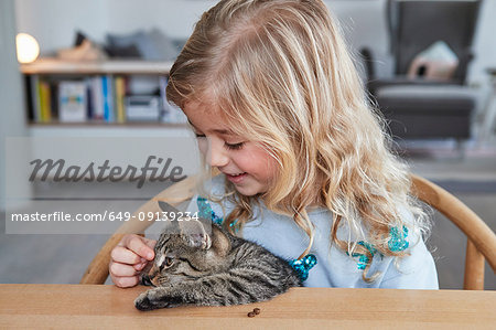 Portrait of young girl, sitting at table, stroking pet cat