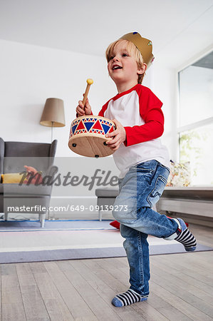 Young boy wearing cardboard crown, beating toy drum, low angle view