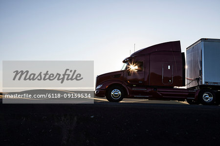 Silhouette of a  commercial truck driving on a highway at sunset.