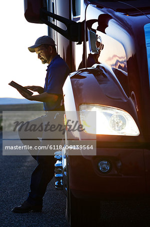 Truck driver checking his notebook computer log while standing next to the cab of his  commercial truck after sunset.