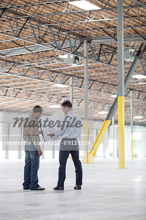 Back man owner of new warehouse and Caucasian man architect going over blue print plans of new interior layout.