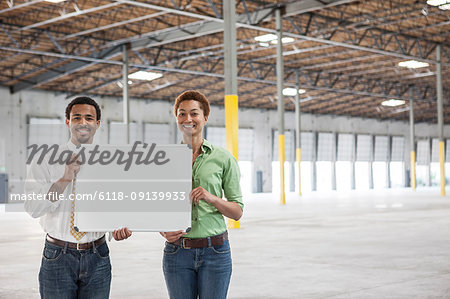 Black man and black woman holding up a blank slate in the interior of a brand new empty warehouse space.