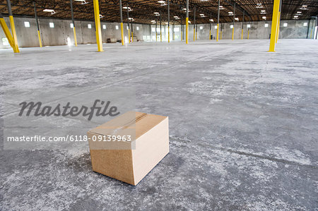 Single cardboard box in the middle of a new empty warehouse space.