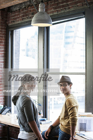 Asian woman and Hispanic man together next to large windows in a creative office.