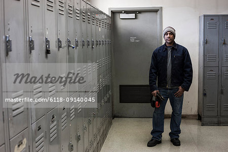 Black man factory worker standing next to lockers in a factory break room.
