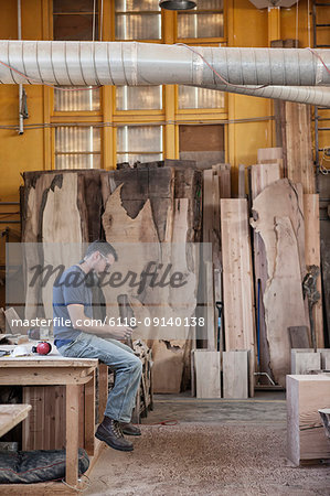 Caucasian man factory worker taking a break checking phone messages in a woodworking factory.